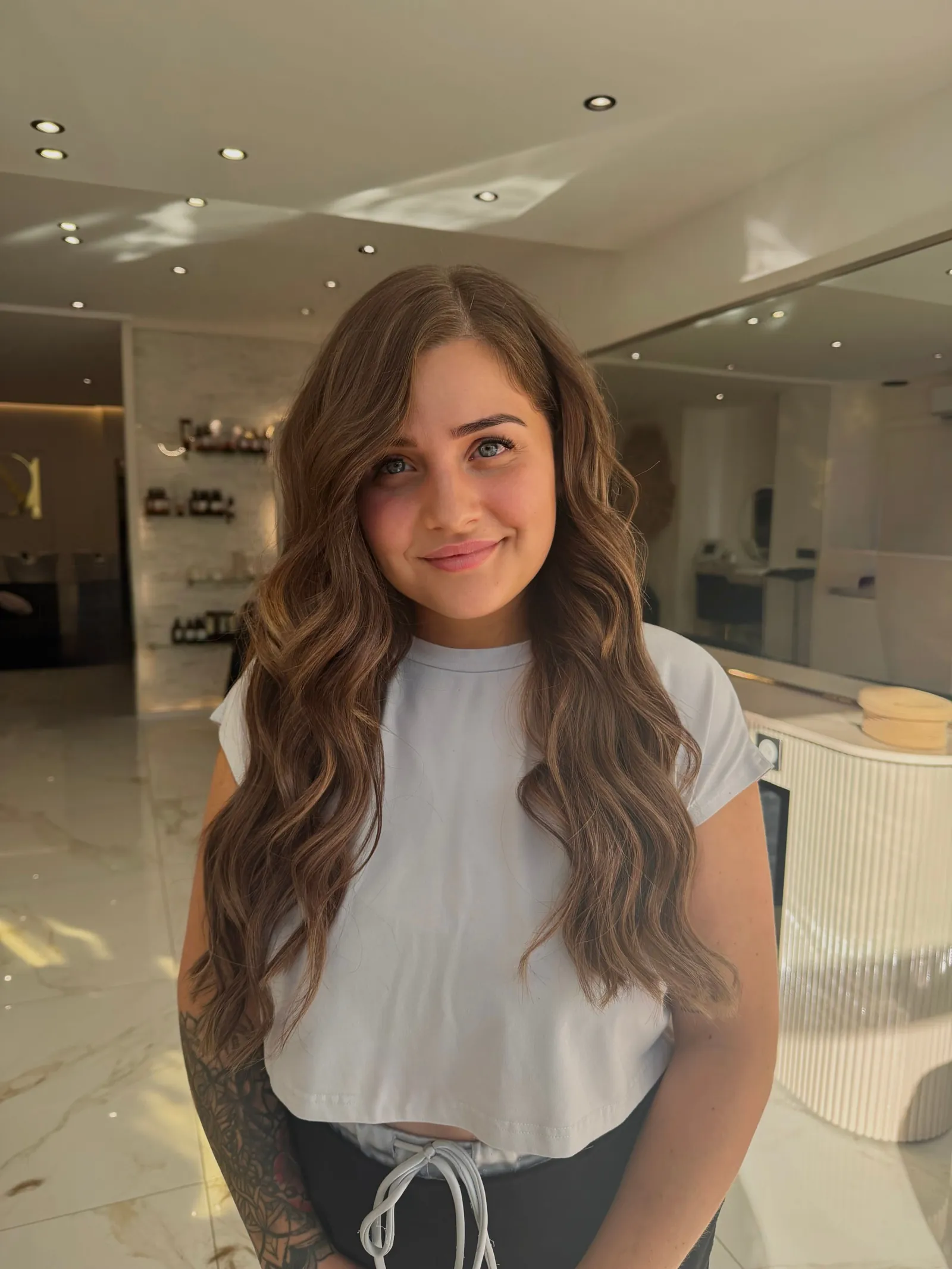 Cliente souriante aux cheveux bruns ondulés, dans le salon aux murs clairs